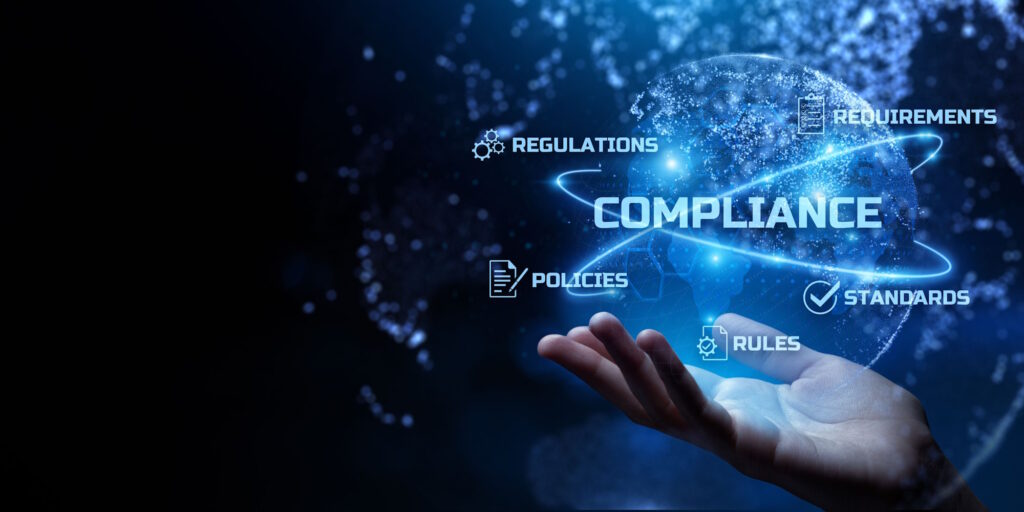 The image shows a holographic sphere hovering over a hand. In the center of the sphere it says compliance. On the outside edges of the sphere is says requirements, regulations, policies, rules, standards