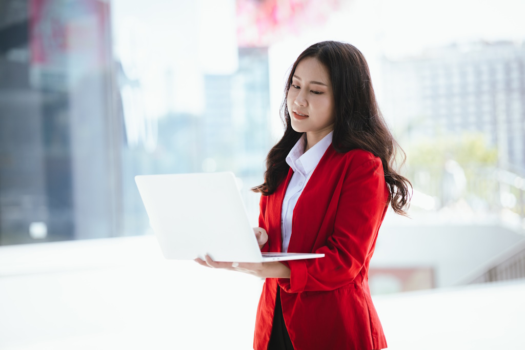 A woman in a red suit is holding a laptop.